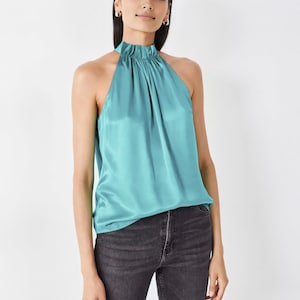 Op de afbeelding: Een turquoise haltertop van satijn met een geplooide halslijn.