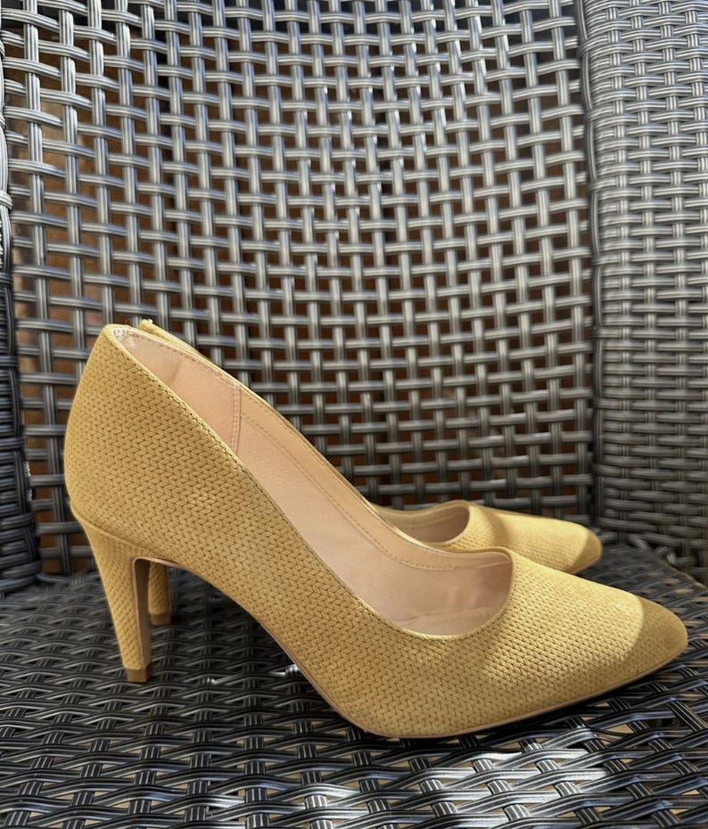 May include: A pair of mustard yellow high-heeled pumps. The shoes have a textured fabric upper, pointed toes, and stiletto heels. The heels measure approximately 3.5 inches.