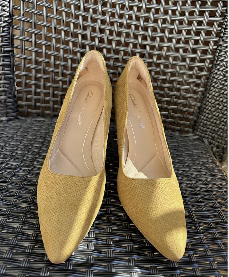 May include: A pair of mustard-yellow Clarks pumps with a textured pattern. The shoes have pointed toes and a low heel. The Clarks logo is visible inside the shoe.