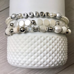 May include: Three white and silver beaded bracelets with the word "BRIDE" spelled out in silver letters.