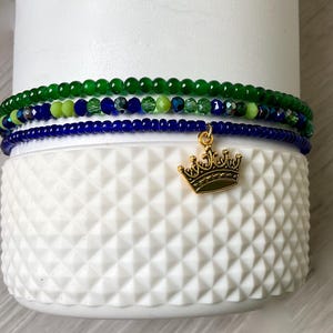May include: Three layered beaded bracelets in green and blue with a gold crown charm.