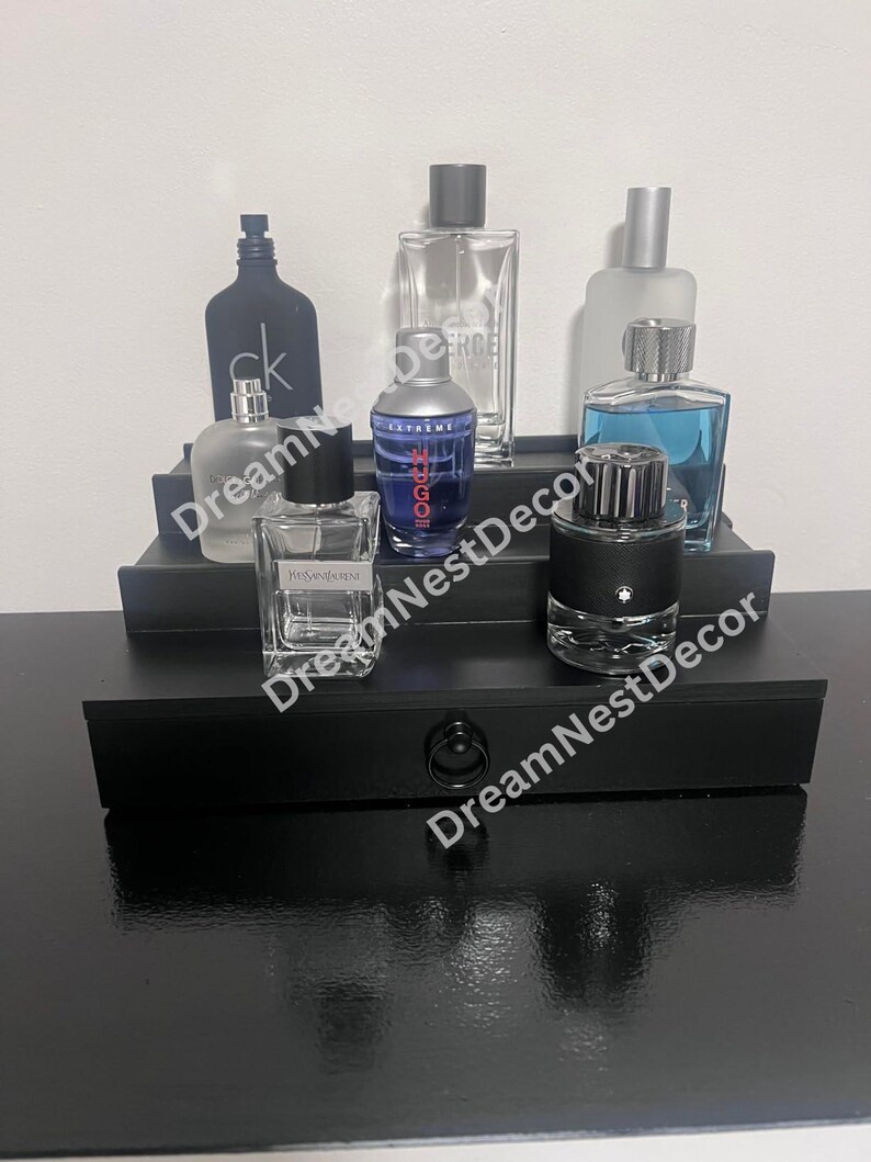 May include: A black tiered shelf display with six glass bottles of cologne. The bottles are arranged in two rows. The top row has three bottles, and the bottom row has three bottles. The bottles are all different sizes and shapes. The shelf is made of wood and has a black finish.