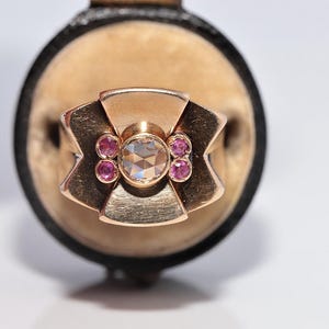 Puede incluir: Un anillo de oro rosa con un diamante central de talla rosa rodeado por cuatro pequeños rubíes redondos de color rosa. El anillo presenta un diseño de banda ancho, geométrico y en forma de abanico con un acabado de metal cepillado.