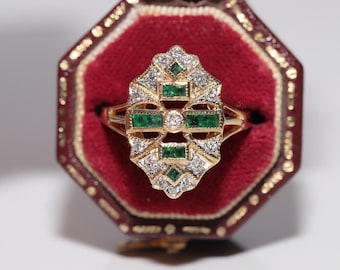 Può includere: Un anello d'oro con un designo di smeraldo verde e diamante. L'anello è in una scatola di velluto rosso.