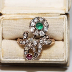 May include: A gold ring with a green emerald and a red ruby set in a floral design with diamonds.