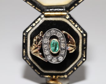 May include: A gold and silver ring with an emerald gemstone surrounded by diamonds. The ring is in a black velvet ring box.