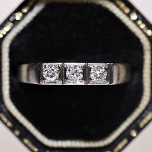 May include: A silver ring with three round diamonds set in a row. The ring is in a black ring box.