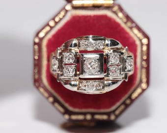 May include: A silver ring with a square-shaped center stone surrounded by smaller diamonds. The ring is set in a red velvet ring box.