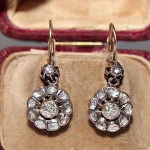 May include: A pair of antique silver earrings with a floral design. Each earring features a round cluster of small diamonds surrounding a larger central diamond.