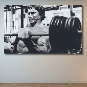 Peut inclure: Photographie en noir et blanc d'un homme soulevant des poids dans une salle de sport. L'homme est musclé et a une expression déterminée sur son visage.