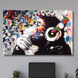 May include: A colorful abstract painting of a monkey wearing headphones with a background of butterflies. The monkey is looking to the left and has a thoughtful expression. The butterflies are in various colors and sizes and are scattered throughout the background.