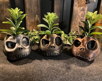 May include: Three black and gold Jack Skellington planter pots with green succulents. The planters are made of ceramic and have a distressed finish.