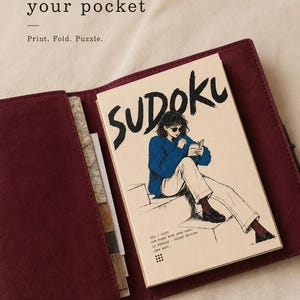 May include: A Sudoku puzzle booklet with a cover illustration of a person in a blue sweater and white pants, tucked into a dark red suede cover. The text reads: made for your pocket, Print. Fold. Puzzle., SUDOKU, 001 / EASY, FOR MINDS WITH OPEN TABS.