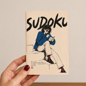 Pode incluir: Um livro de Sudoku retangular com capa cor de creme apresentando uma ilustração em tinta preta de uma pessoa de suéter azul e calças claras sentada escrevendo. O texto diz SUDOKU, 001 / EASY, FOR MINDS WITH OPEN TABS, 25 PUZZLES - POCKET EDITION, LEAN DEPT.