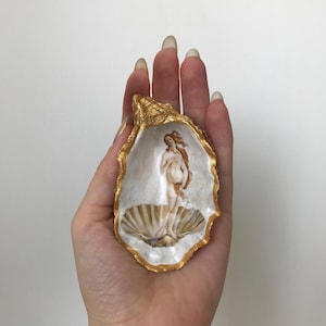 May include: A gold-painted oyster shell with a painting of the Birth of Venus inside. The painting is a miniature version of the famous Renaissance artwork.