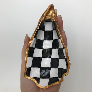 Puede incluir: Una concha de mar con borde dorado y un patrón de tablero de ajedrez en blanco y negro en el interior.