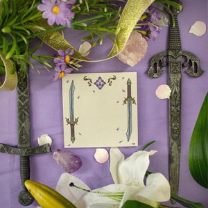 May include: A white card with two silver swords with blue and gold accents on a purple background with white flowers and green leaves. The card has a purple flower with a gold centre in the top centre.