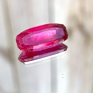 May include: A deep pink, faceted gemstone with a rectangular shape.