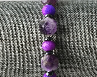 May include: A beaded bracelet featuring faceted amethyst and vibrant purple beads. The bracelet includes small, dark gray spacer beads. The gemstones are strung together, creating a striking contrast of colors and textures. This jewelry piece is a stylish accessory.