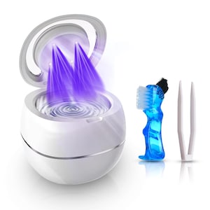 Può includere: Un sterilizzatore UV bianco a forma di uovo con un coperchio aperto che emette luce viola. Uno spazzolino blu e una pinzetta bianca sono a destra. Lo sterilizzatore ha un bordo argentato e un interno ondulato.
