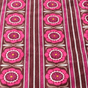 May include: A patterned fabric with a repeating floral design. Large pink flowers with yellow centres are interspersed with vertical stripes in brown, pink, and white. The design has a retro aesthetic, reminiscent of the 1970s.