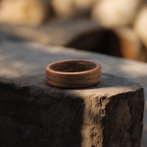 May include: A handcrafted wooden ring with a natural, warm brown color. The ring is made from a single piece of wood, showcasing the grain pattern. The ring is a simple band, perfect for everyday wear.