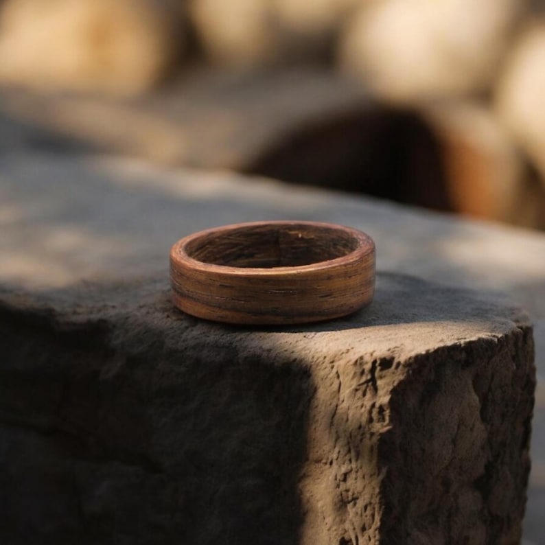 May include: A handcrafted wooden ring with a natural, warm brown color. The ring is made from a single piece of wood, showcasing the grain pattern. The ring is a simple band, perfect for everyday wear.