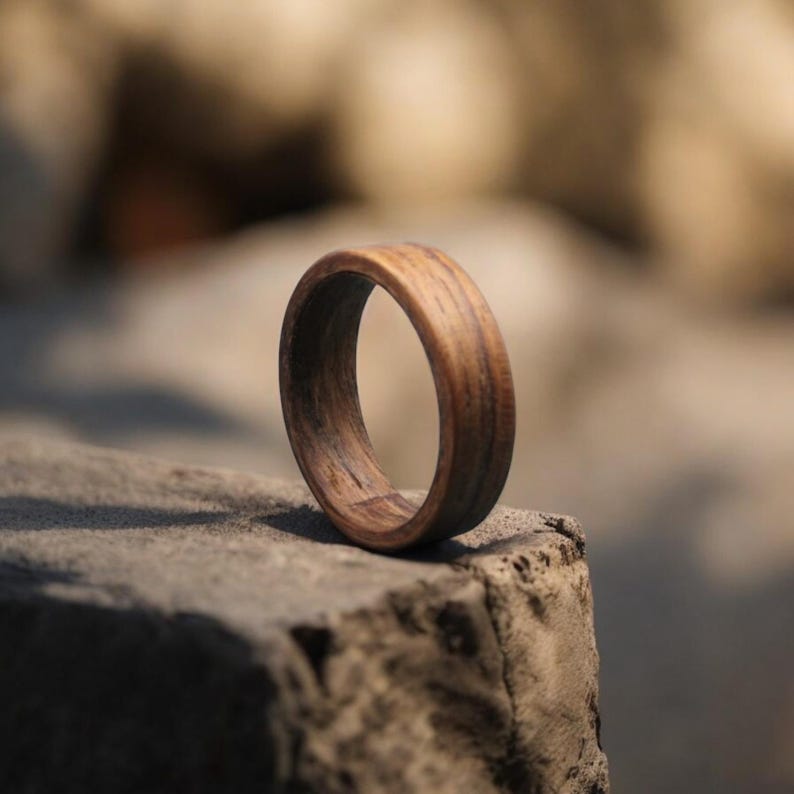 May include: A handcrafted wooden ring with a rich, dark brown color. The ring is made from a single piece of wood, showcasing the natural grain and texture. The ring is a simple band design.