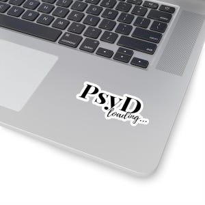 Könnte beinhalten: Ein weißer Aufkleber mit dem Text "PsyD loading..." in Schwarz, platziert auf einem silbernen Laptop. Die Schriftart des Aufklebers ist eine Mischung aus Serifen- und Schreibschriftstilen. Die Laptop-Tastatur ist im Hintergrund sichtbar.