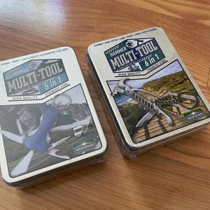 May include: Two metal boxes containing multi-tools. One box reads "All-Purpose Multi-Tool 5 in 1 Stainless Steel" and features a blue and silver multi-tool. The other box reads "Hammer Multi-Tool 6 in 1 Stainless Steel" and shows a silver multi-tool with a hammer.