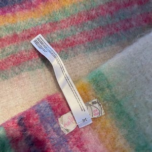 Op de afbeelding: Een veelkleurig gestreept textiel in roze, blauw, geel en groen. Een wit label met tekst is aan het textiel bevestigd. Het label heeft een kleine illustratie en het woord "Free People".