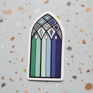 May include: A sticker of a stained glass window with a blue, green, and white color scheme. The window is arched and has a geometric design.
