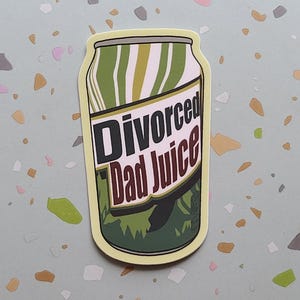 May include: A sticker in the shape of a soda can with the words "Divorced Dad Juice" in a bold, brown font. The can design features green and white vertical stripes and a green, leafy base. The sticker has a yellow border.
