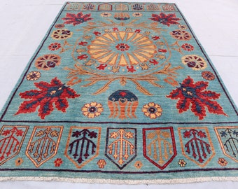 May include: A teal blue rug with a central medallion featuring a sunburst design. The rug has a border with stylized floral and leaf motifs in shades of red, yellow, and blue.