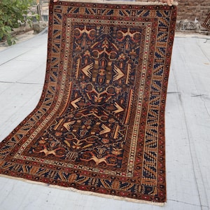May include: An intricately patterned rug with a dark blue field, bordered by red and tan designs. The rug features geometric and stylized floral motifs in shades of tan, brown, and red. The rug is rectangular.