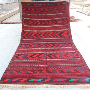 May include: A red, blue, and white patterned rug with a fringe border. The rug has a geometric design with repeating patterns.