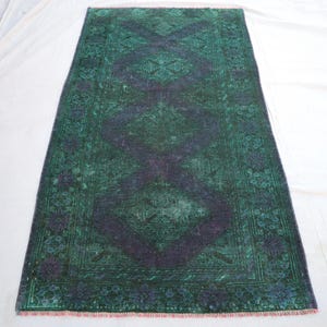 Puede incluir: Alfombra rectangular de aspecto envejecido en tonos verdes y morados. Presenta un diseño central de rombos y un borde floral. La alfombra mide aproximadamente 91 x 183 cm.