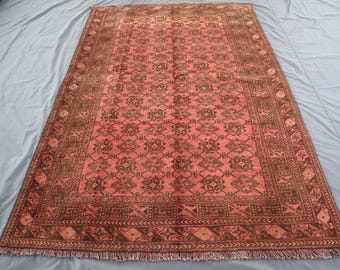 Könnte beinhalten: Ein rechteckiger, handgewebter Teppich mit einem zentralen Feld aus rötlichem Rosa und aufwendigen braunen Blumenmustern. Der Teppich hat einen detaillierten Rand mit geometrischen Designs und einen Fransenrand. Die Abmessungen des Teppichs sind nicht sichtbar.