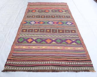 May include: A colorful, striped rug with a geometric pattern. The rug is made of woven fabric and has a fringe border.