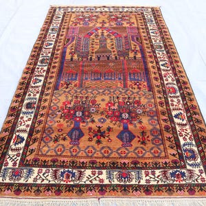 Può includere: Un tappeto da preghiera tradizionale con sfondo marrone e intricati motivi floreali e geometrici in tonalità di rosso, blu e bianco. Il tappeto ha un bordo con frange.