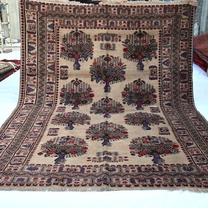 May include: A rectangular beige rug with a repeating pattern of stylized trees in vases, framed by a detailed border. The trees feature red and blue floral elements. The rug is displayed on a white surface.