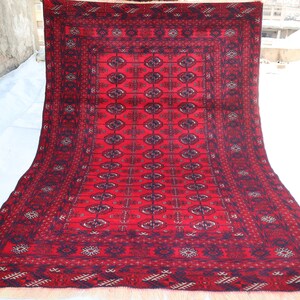 May include: A red and blue patterned rug with a traditional design. The rug has a fringe border and is made of wool.