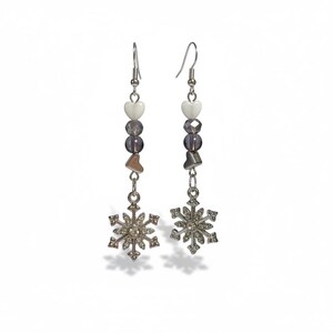 May include: A pair of dangle earrings with snowflake charms. Each earring features a silver-tone snowflake pendant, heart-shaped and round beads in white and gray, and a silver fish hook.