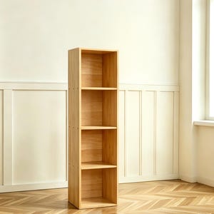 May include: A tall, light-colored wooden bookshelf with four shelves. The bookshelf is made of natural wood and has a simple, modern design. It stands on a wooden floor and is against a white wall.