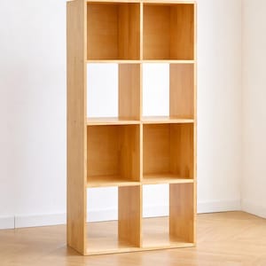 May include: A light-colored, eight-cube wooden bookshelf. The bookshelf is rectangular and stands upright, with four shelves across and two shelves high. The wood has a natural finish, and the unit is empty.