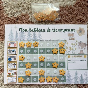 Peut inclure: Un tableau de récompenses avec le texte "Mon tableau de récompenses" et des illustrations d'animaux de la forêt. Comprend des jetons en forme d'étoiles dans un sac transparent. Le tableau a des espaces pour les tâches quotidiennes et les récompenses.
