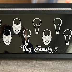May include: A black framed display with the text "Vwj Family Est 1981" and nine silver necklaces with different designs. The necklaces are displayed on a black background.
