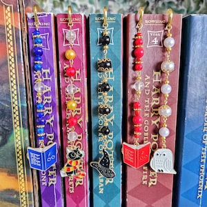 May include: Beaded Harry Potter-themed bookmarks with gold-colored hooks. Each bookmark features a charm, including an open book, a cat in a scarf, a wizard hat, and an owl. The beads are in various colors, including blue, red, yellow, black, and white.