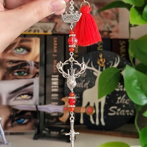 Puede incluir: Marcapáginas decorativo plateado con cuentas rojas, borla roja y dije de corona. El marcapáginas también presenta un colgante de cabeza de ciervo y un dije de espada, para amantes de los libros.