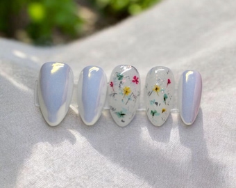 May include: Set of six oval-shaped press-on nails with a pearly white base and a floral design. The flowers are small and colourful, with white, yellow, pink, and green accents.